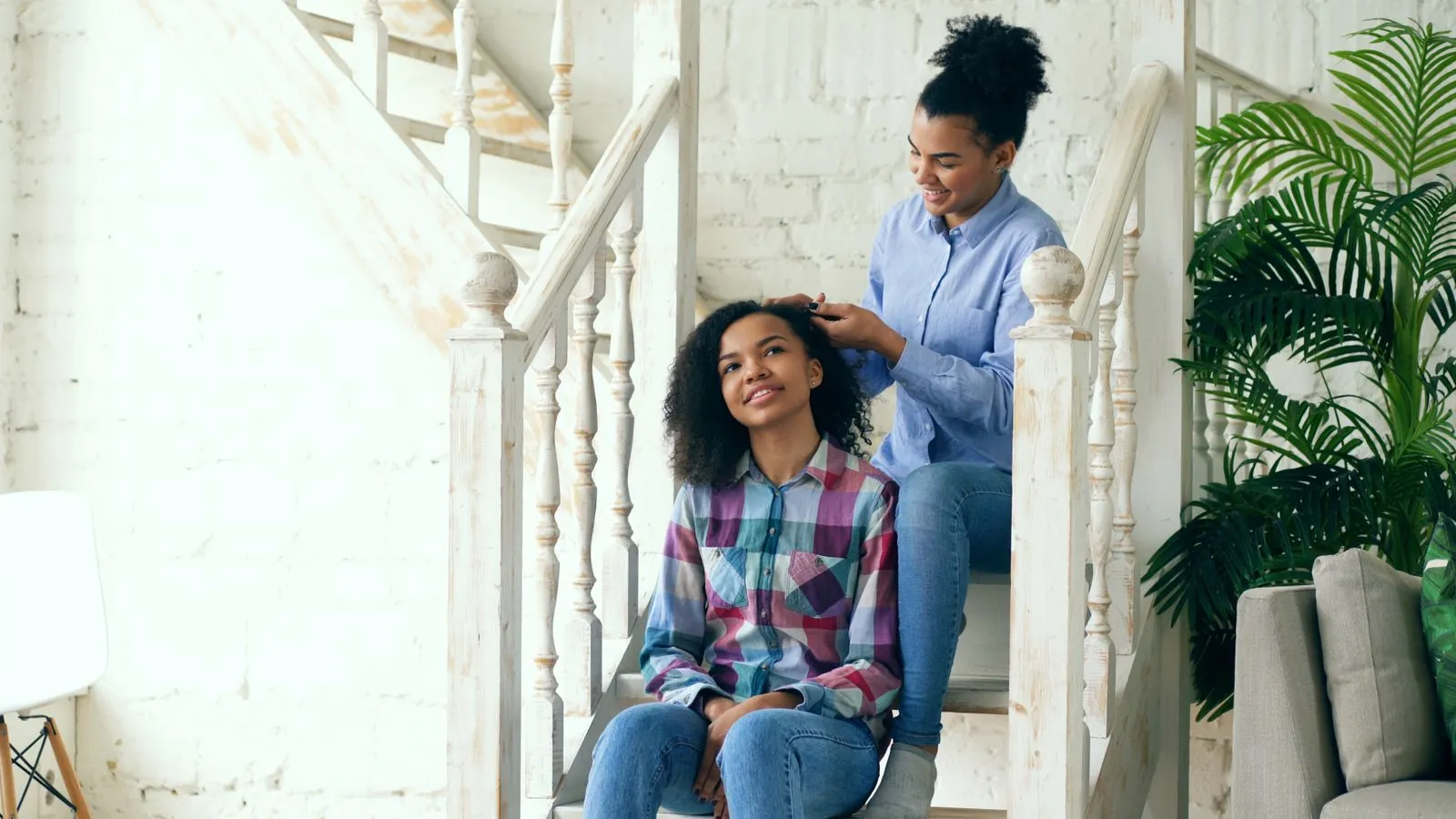 Two women enjoy a hair styling session on staircase indoors, fostering a sense of friendship and relaxation.